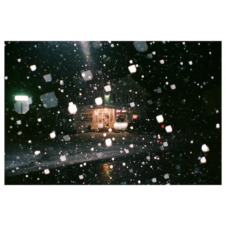 A building with illuminated windows is seen through falling snow at night.