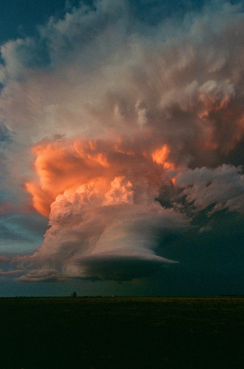 A large, dramatic cloud formation with orange and grey hues looms over a dark, flat landscape.