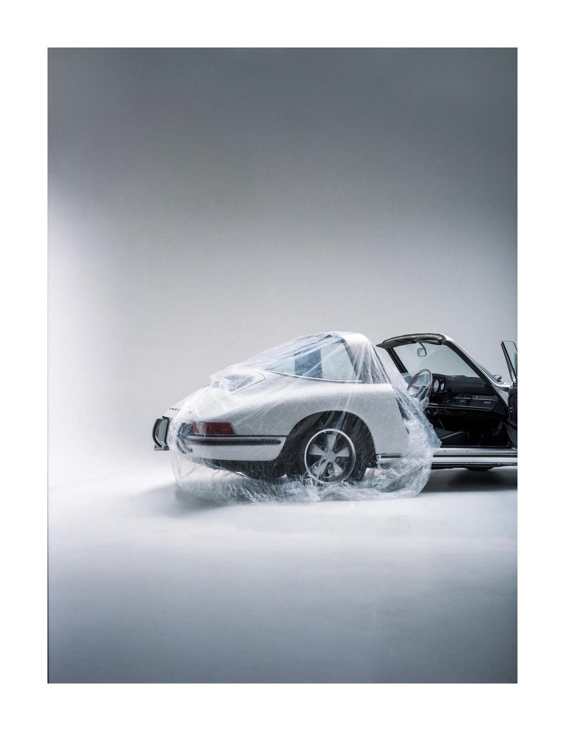 A white vintage car is partially covered in clear plastic sheeting with its door open.