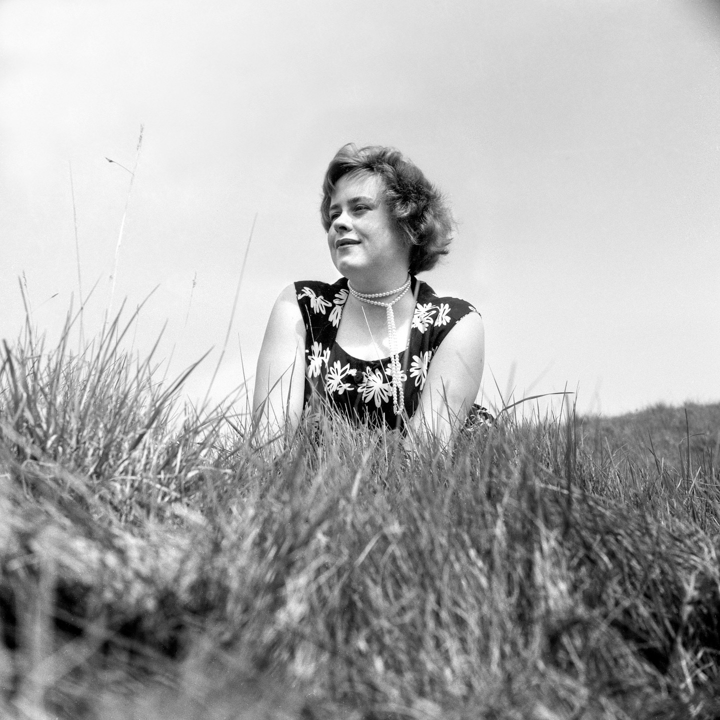 A young woman with a pearl necklace is lying in tall grass.