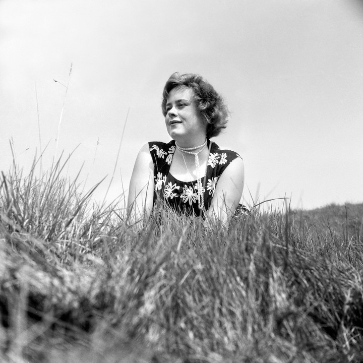 A young woman with a pearl necklace is lying in tall grass.