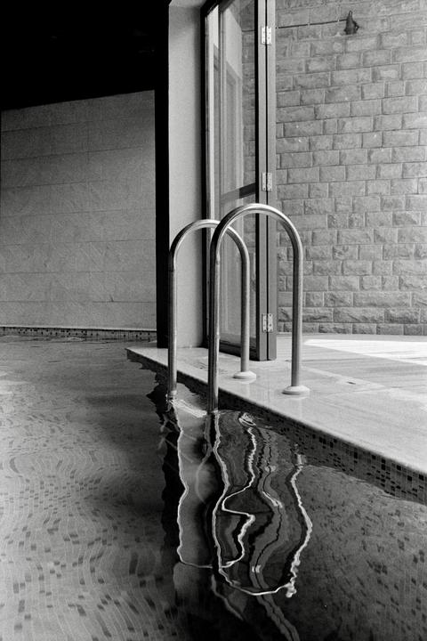 Two metal handrails extend into a swimming pool with a tiled edge, reflecting in the rippling water.