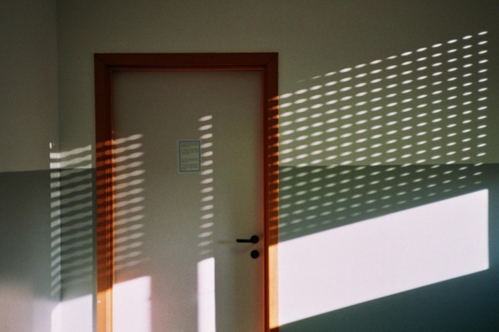 Sunlight streams through blinds, casting shadows on a door and wall.