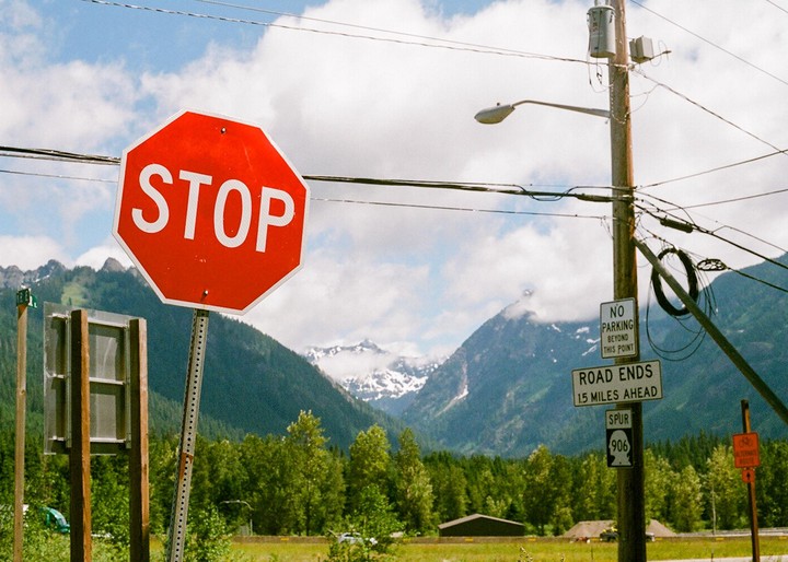 A red stop sign stands prominently in the foreground with a mountain range and forest in the background.