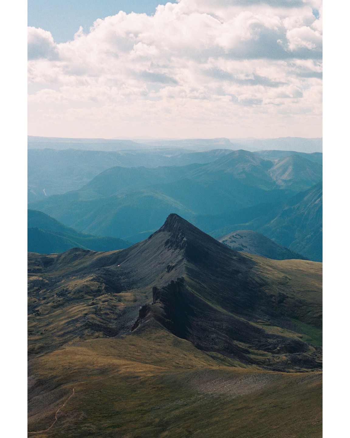 A mountain peak rises above a vast landscape of rolling hills under a cloudy sky.