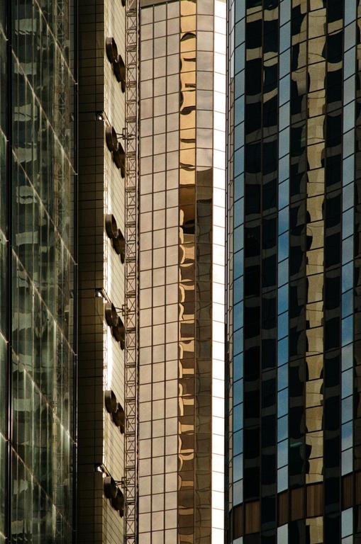 The glass facade of a modern building reflects the sky and other structures.