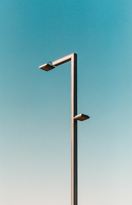 A tall, modern street light with two lamps extends upwards against a clear blue sky.