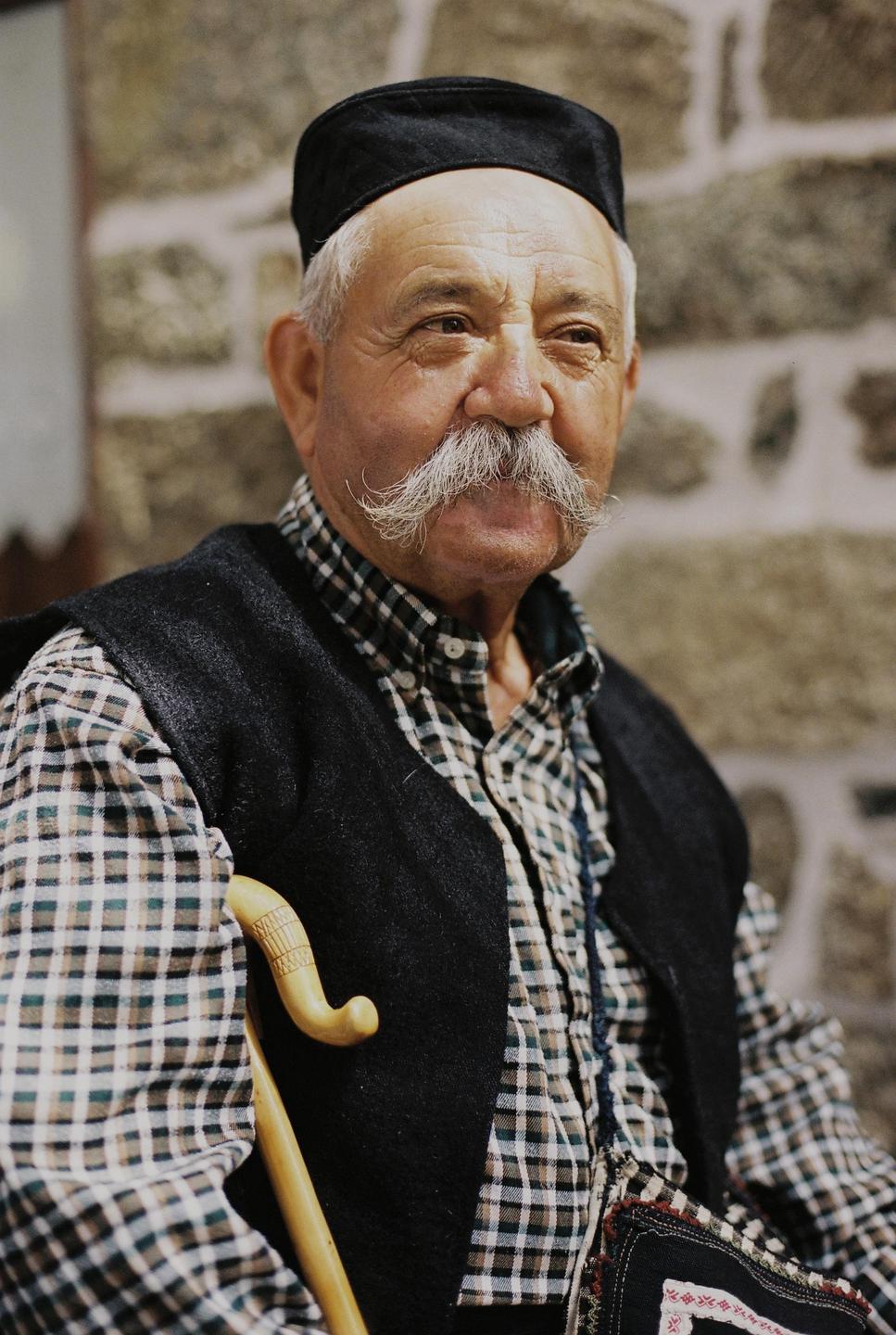 A man with a large white mustache and a black cap is looking to the right.