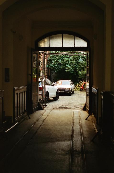 A dark hallway opens to a sunlit courtyard with two cars and a scooter.