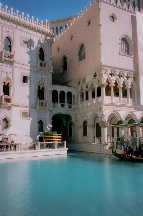 A gondola with a gondolier and passengers floats on a canal next to ornate buildings.