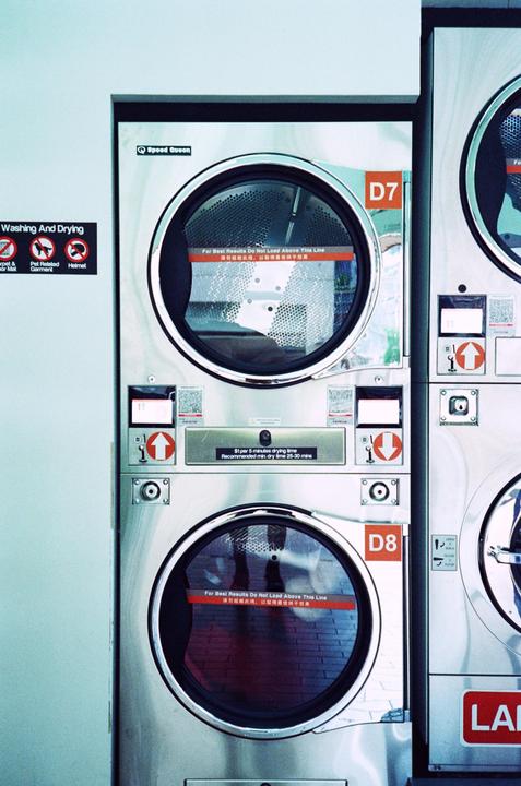 Two stacked washing machines are visible in a laundromat with a sign on the wall.