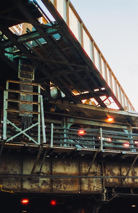 A low-angle view shows the underside of an elevated train track with red lights and exposed wiring.