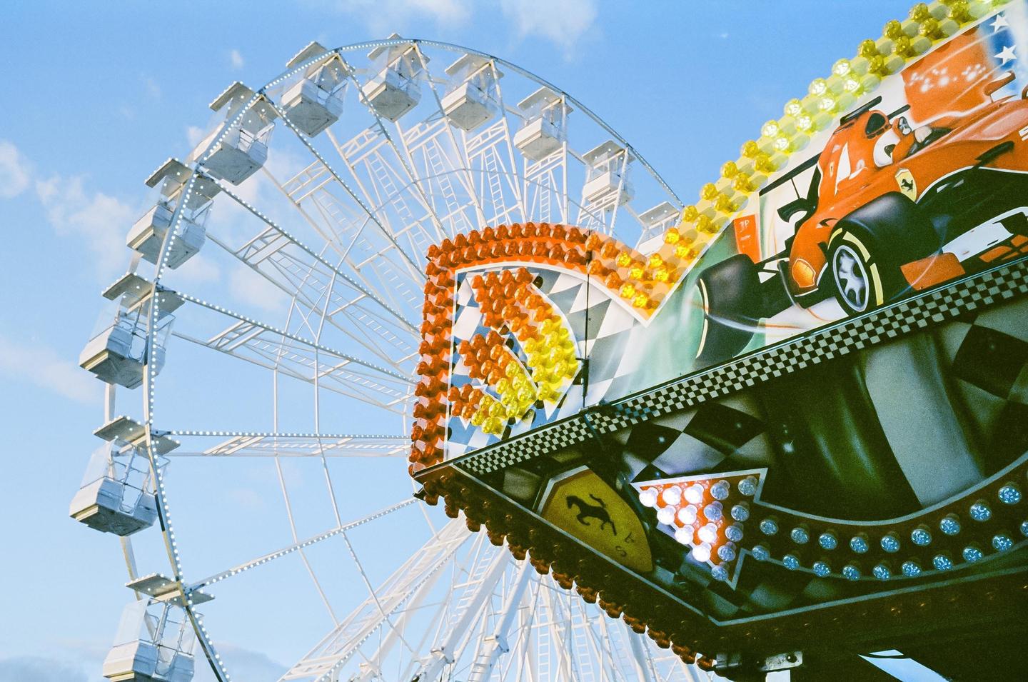 A ferris wheel and a funfair ride with a race car graphic are visible against a blue sky.