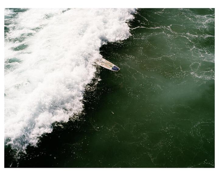 A surfboard is visible next to a large breaking wave in the ocean.