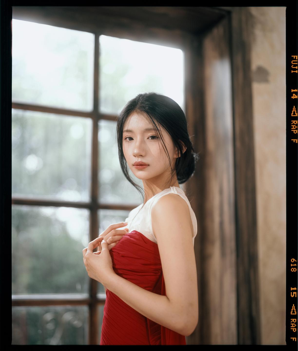 A woman in a red dress stands in front of a window.