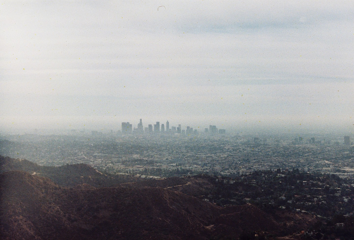 A hazy view of the Los Angeles skyline is visible over hills and a sprawling city.