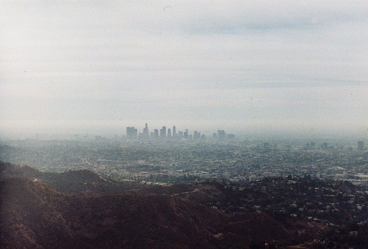 A hazy view of the Los Angeles skyline is visible over hills and a sprawling city.