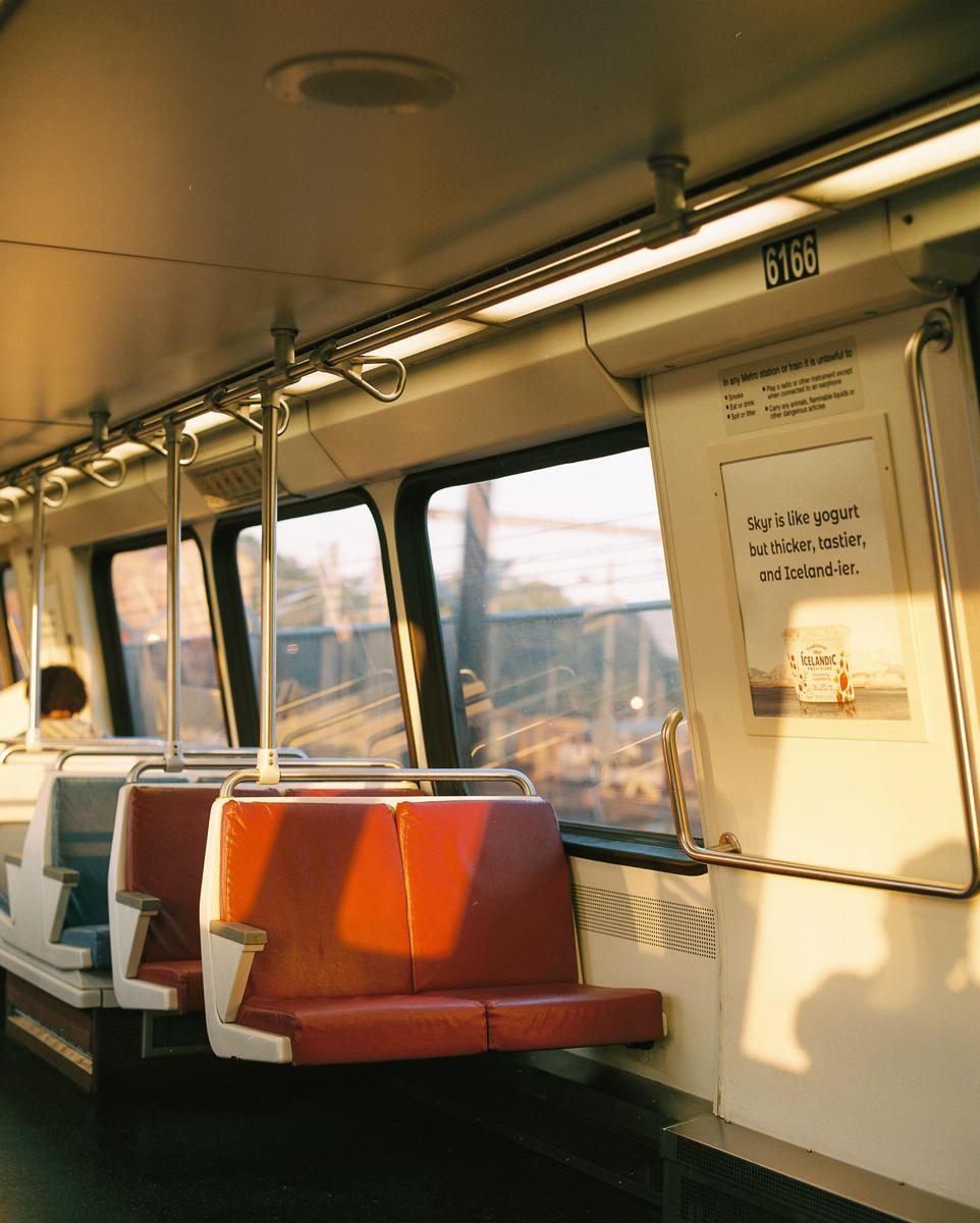 Sunlight streams through the windows of a metro car, illuminating red seats and an advertisement.