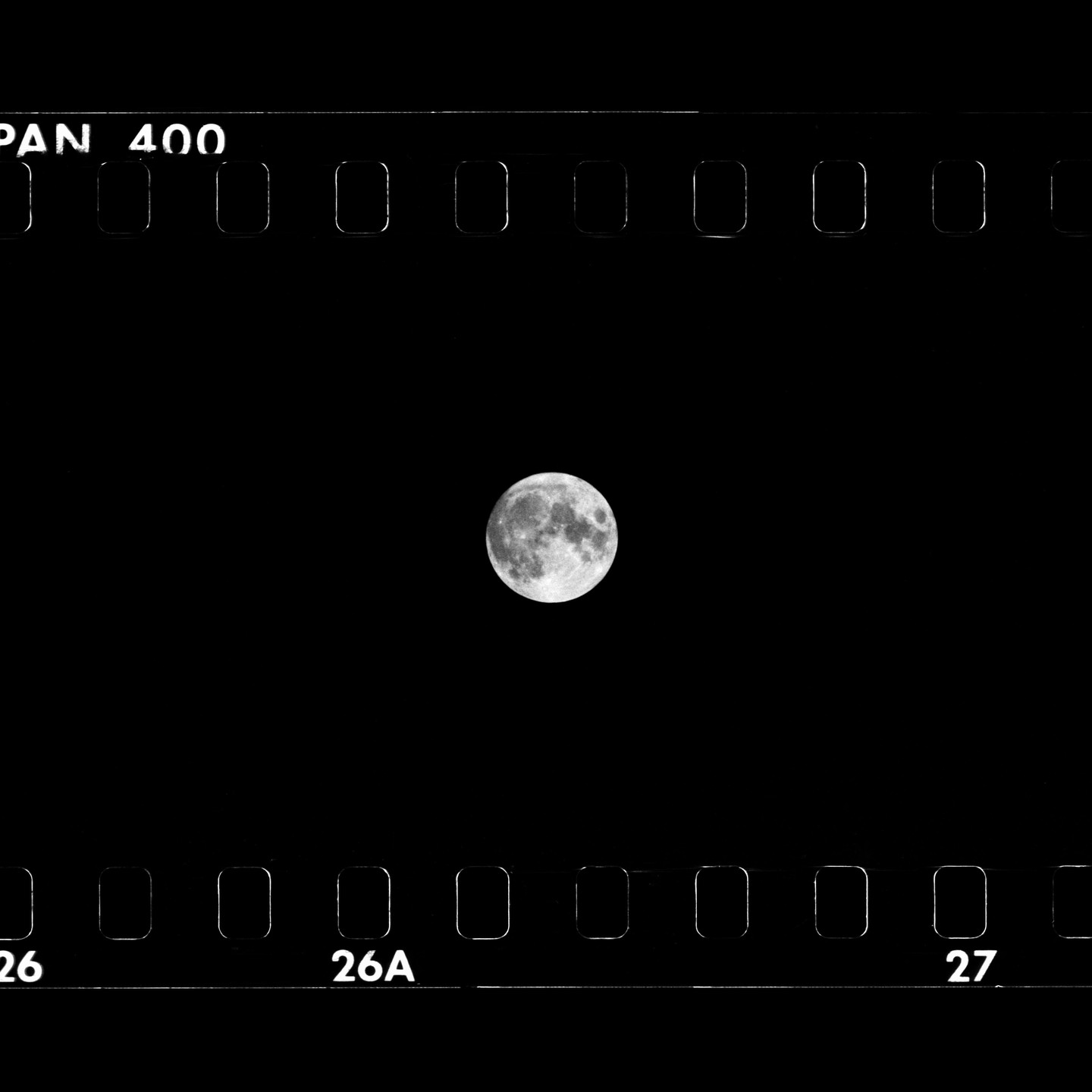 A full moon is centered in a black sky, framed by the sprocket holes and edge markings of a film strip.