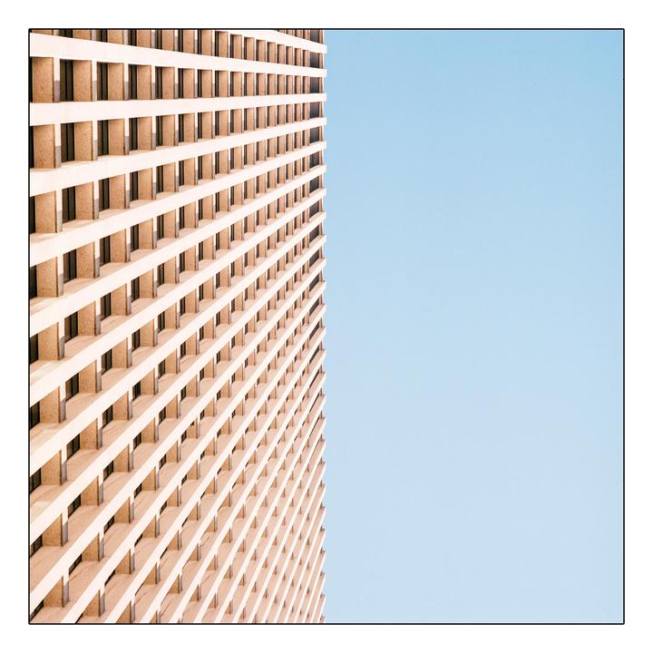 A tall building with a grid-like facade stands against a clear blue sky.