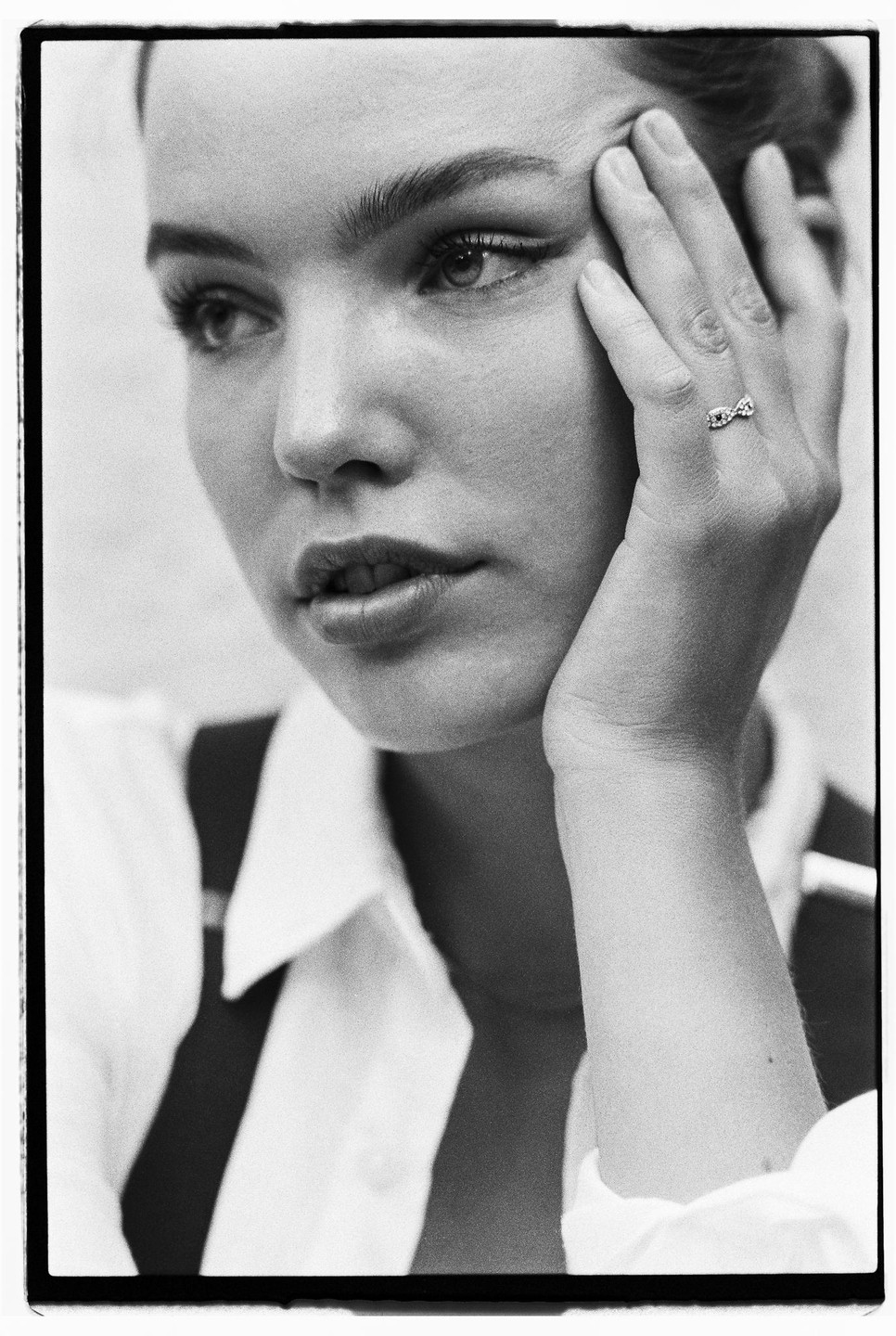 A woman with a ring on her finger rests her hand on her face and looks away from the camera.