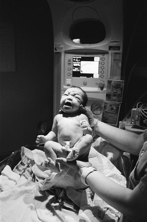 A newborn baby is held by a person wearing gloves, with medical equipment in the background.