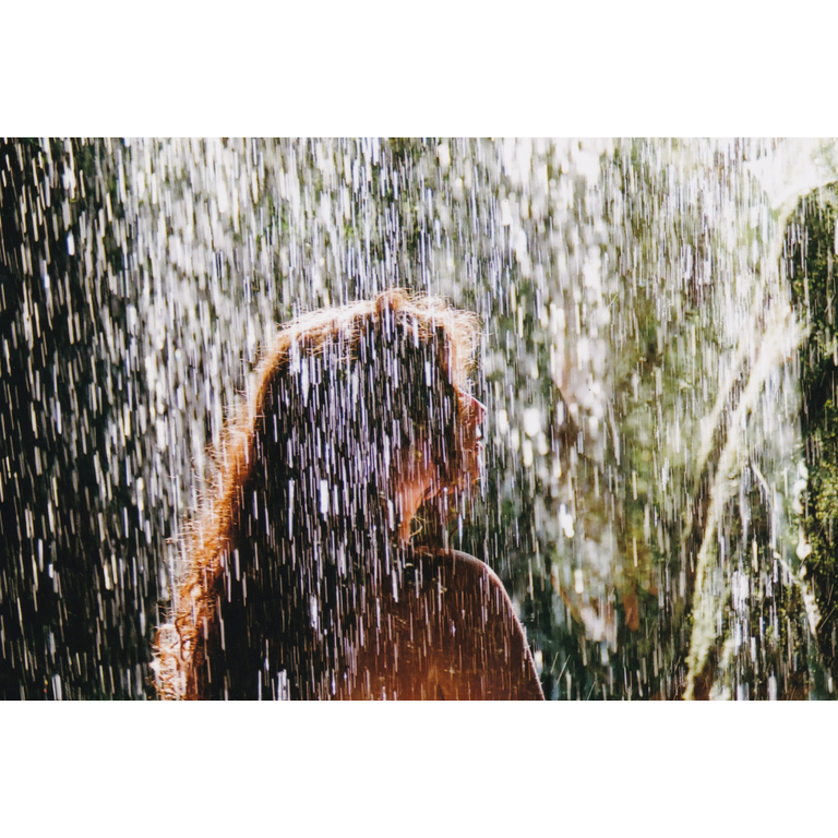 A woman with long, curly hair stands in the rain, looking to the right.