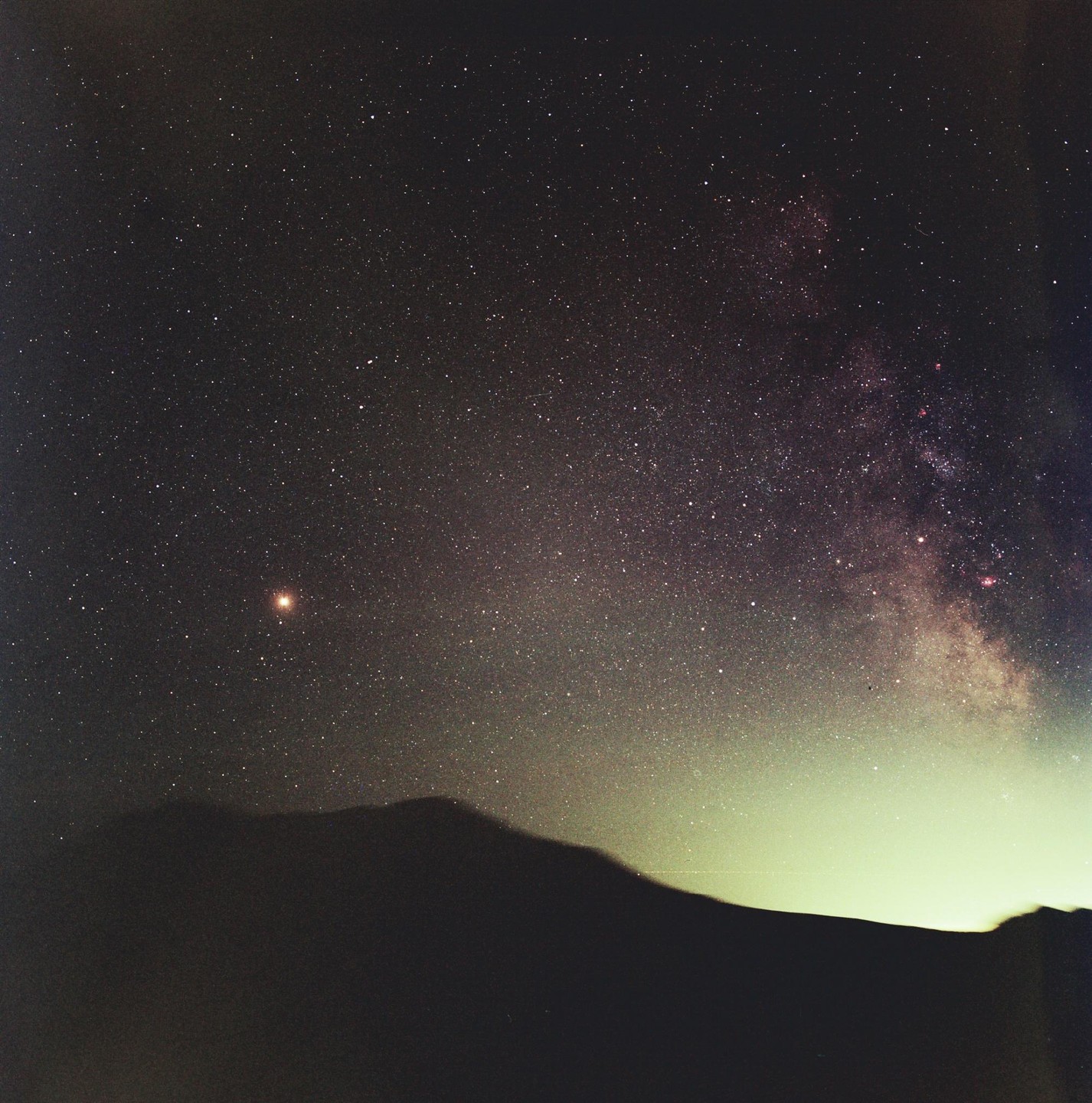 A mountain range is silhouetted against a night sky filled with stars and the Milky Way.
