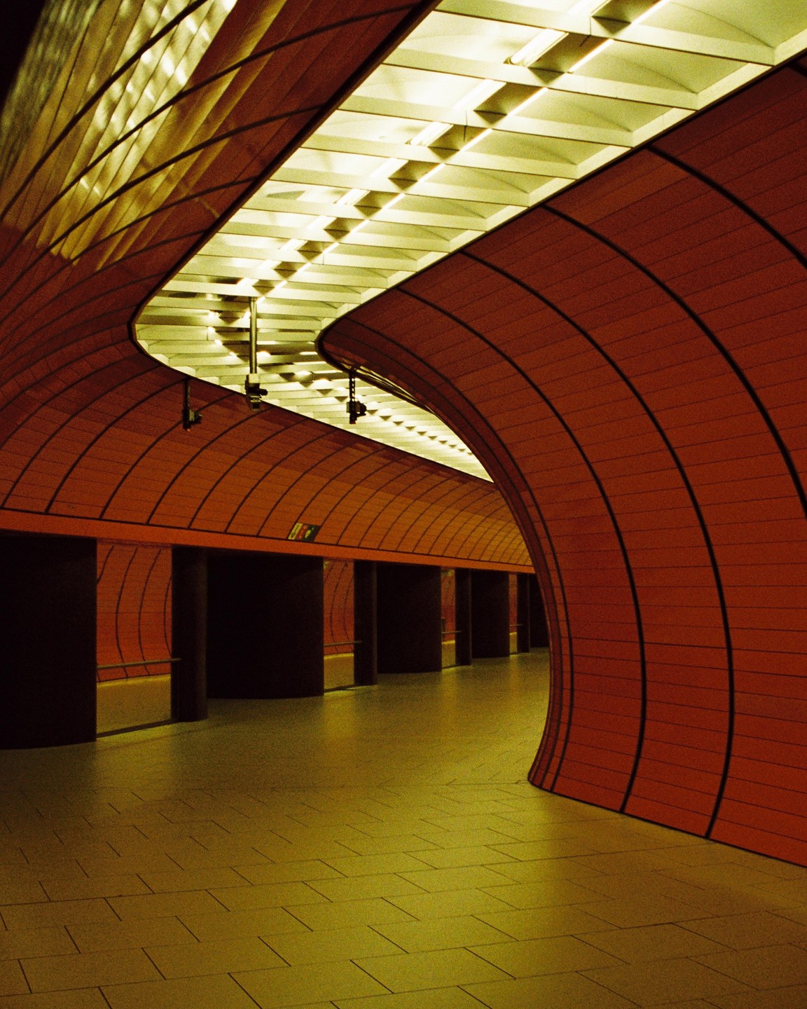 A long, empty, curved subway tunnel is lit by overhead fluorescent lights.