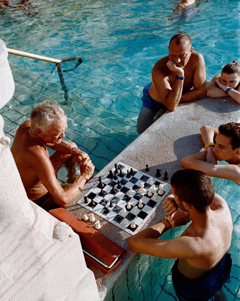 Four people are playing chess in a swimming pool on a sunny day.