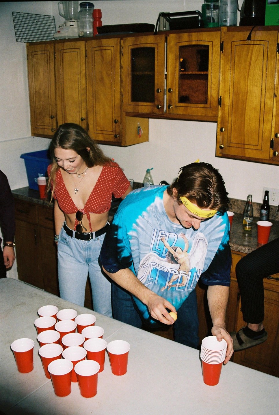 A man and a woman are playing beer pong in a kitchen.