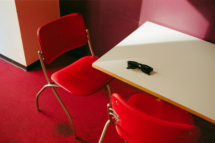 A pair of sunglasses rests on a white table next to two red chairs on a red carpet.