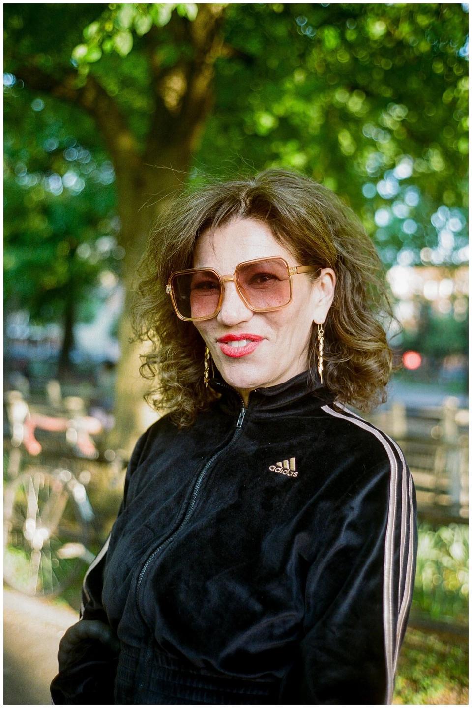 A woman wearing sunglasses and a black track jacket smiles at the viewer.