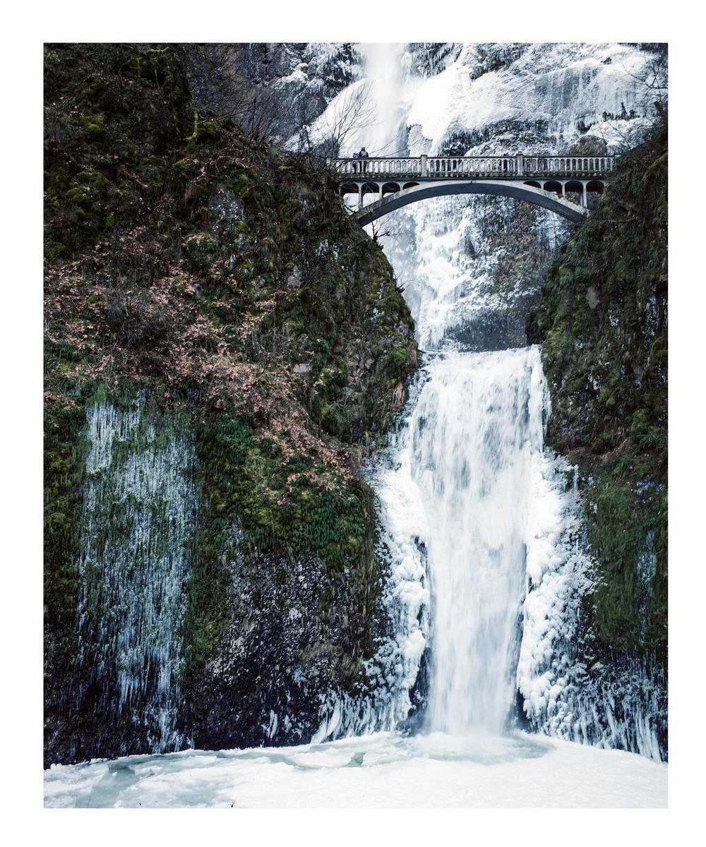 A bridge spans a frozen waterfall with icy cliffs on either side.