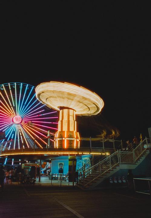 A brightly lit Ferris wheel and a spinning carnival ride illuminate the night sky at an amusement park.