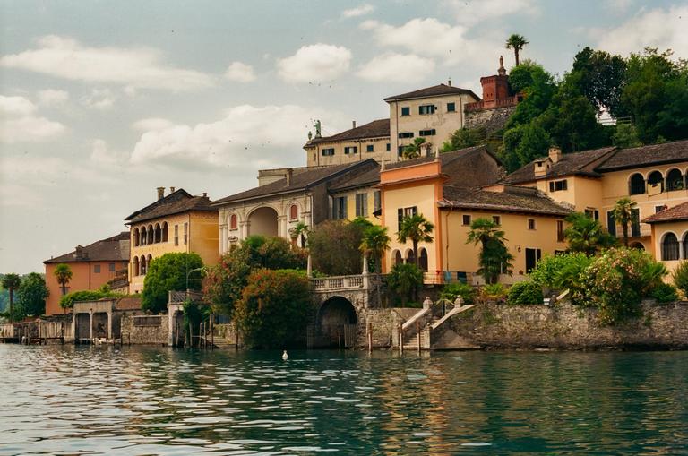 A town with buildings of various colors and styles is built into a hillside overlooking a lake.