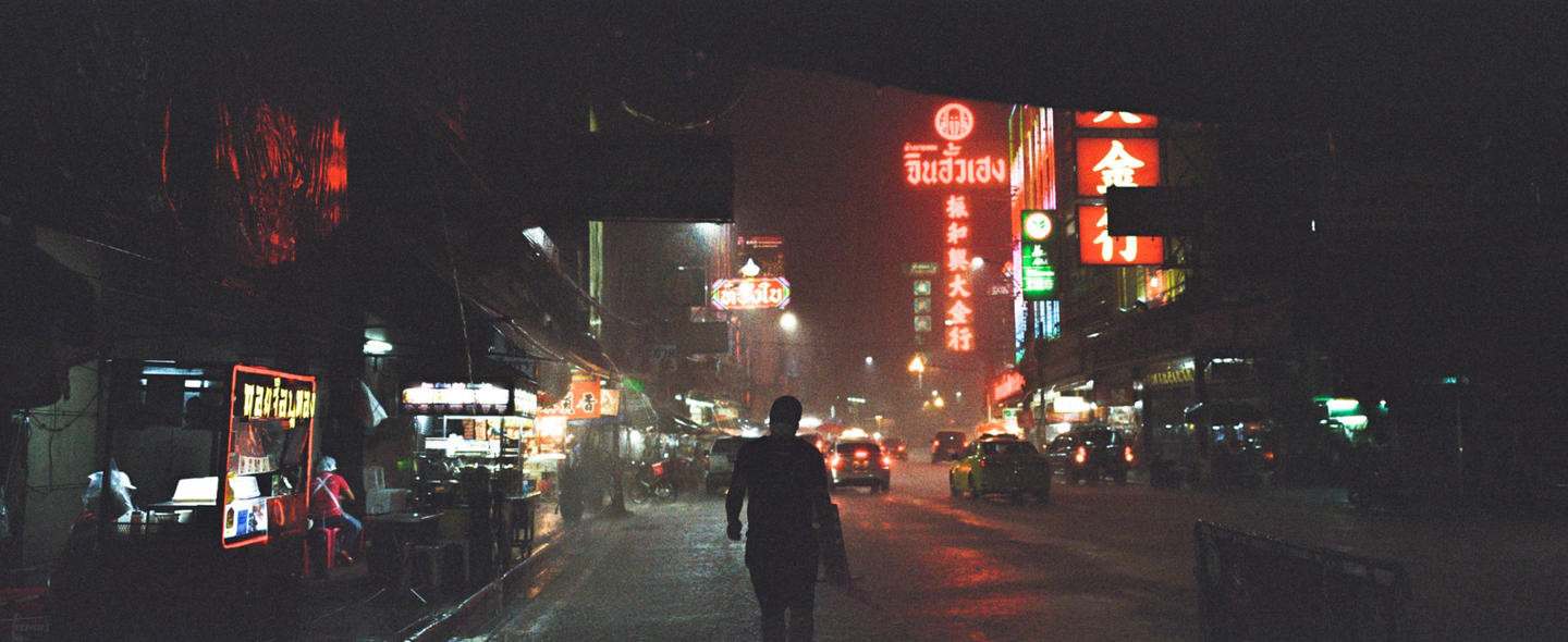A person walks down a street at night with neon signs and cars.
