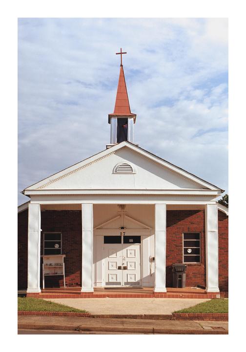 A brick church with a white facade and a red steeple stands under a cloudy sky.