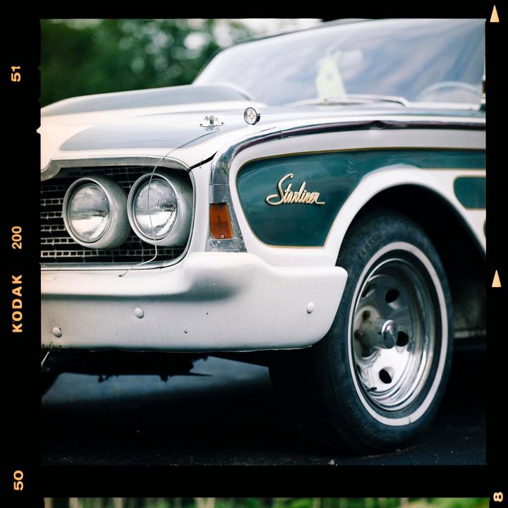 A close-up shot shows the front of a vintage car with its headlights and grille visible.