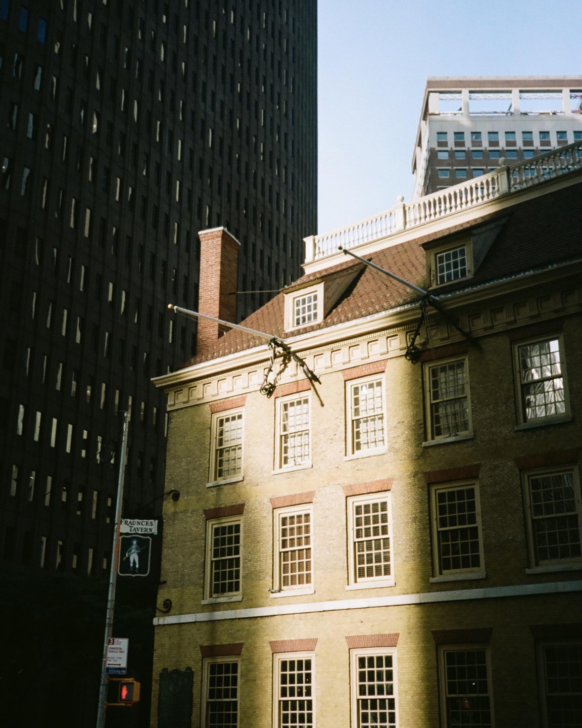 A historic building with a red brick chimney stands next to a modern skyscraper, with sunlight illuminating part of its facade.
