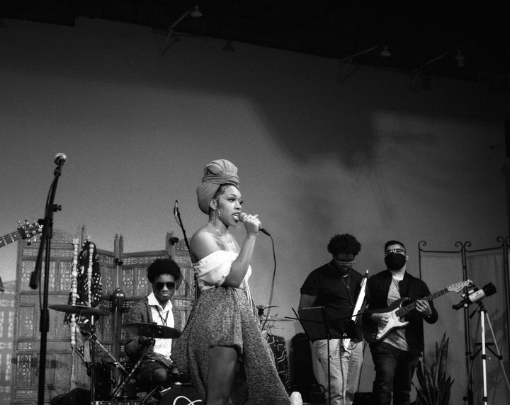 A woman sings into a microphone on a stage with a band.