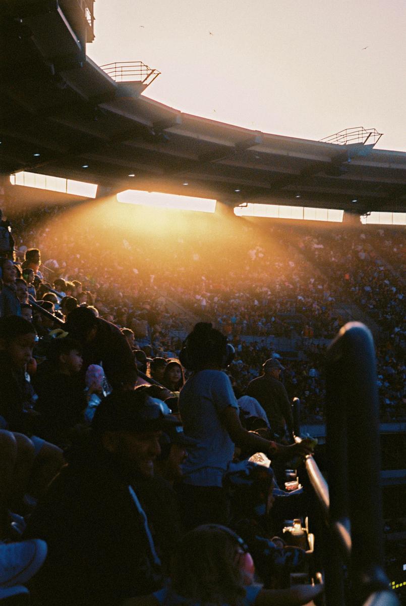 A crowd of people sits in a stadium as a bright light shines from above.