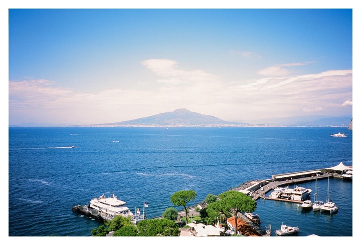 A wide shot shows a body of water with a mountain in the distance and a dock with boats in the foreground.