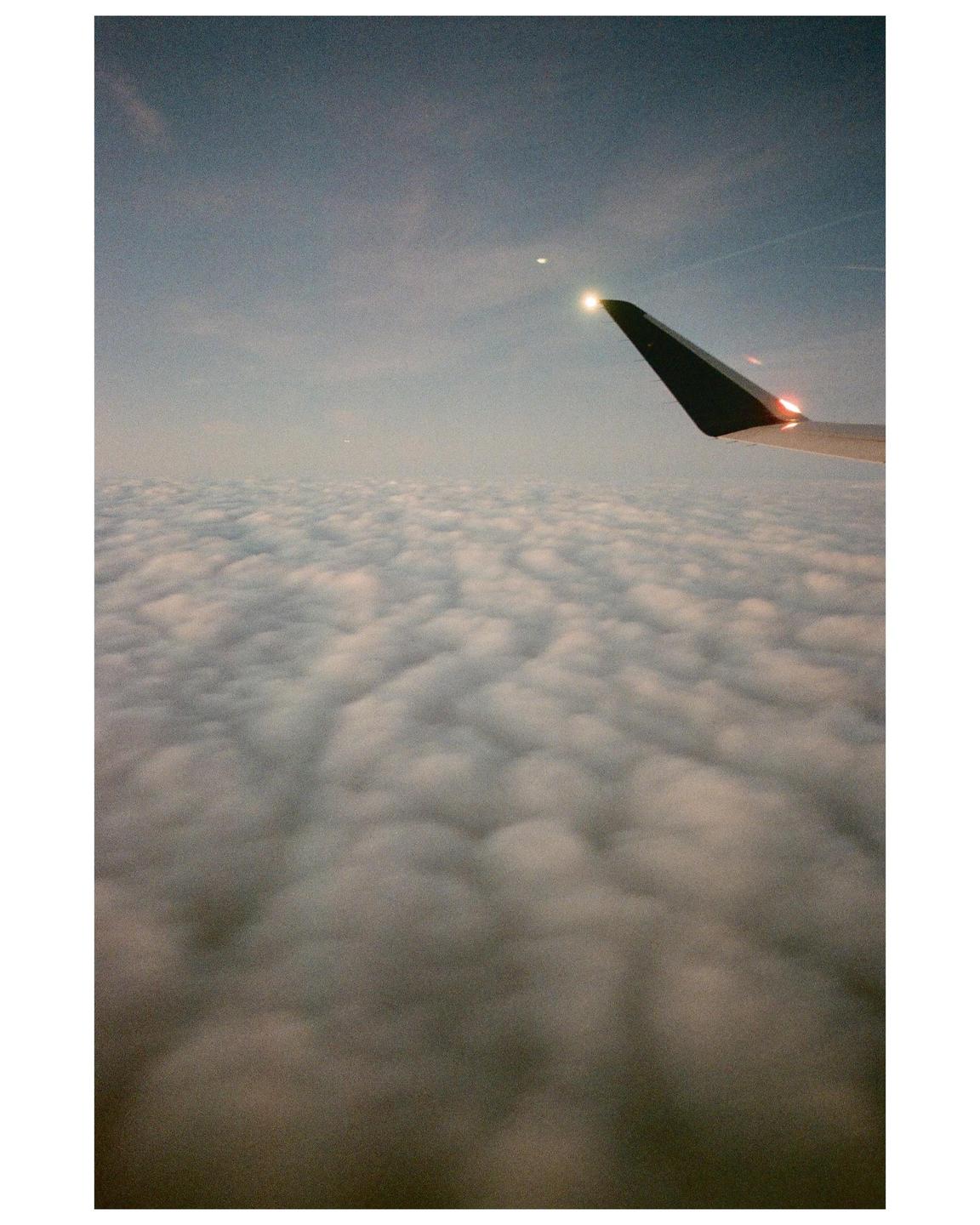 An airplane wing is visible above a vast expanse of clouds under a hazy sky.