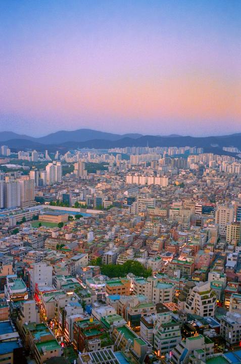 An aerial view of a city with mountains in the distance under a colorful sky at dusk.
