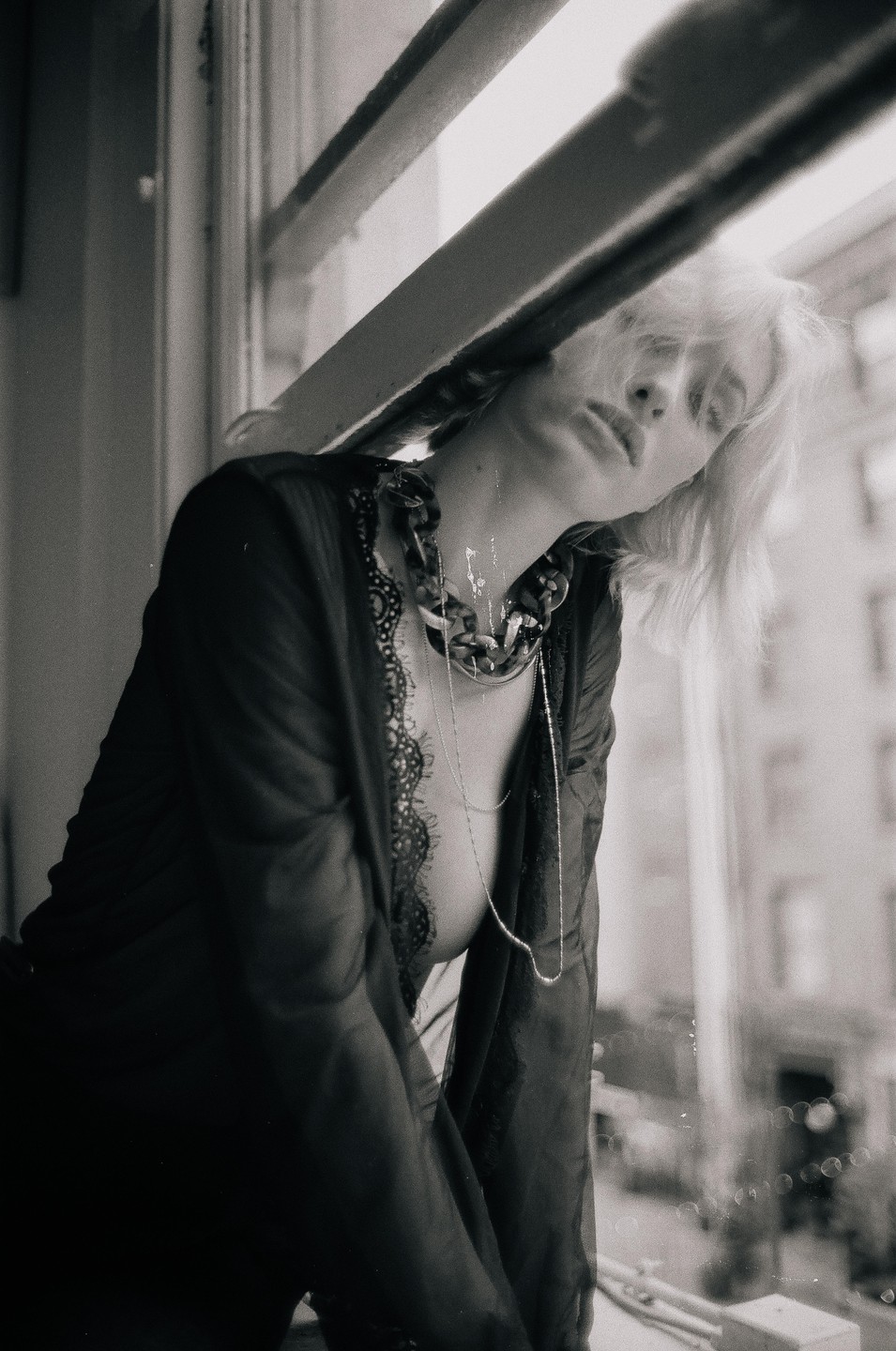 A woman with blonde hair and a sheer robe leans out of a window.