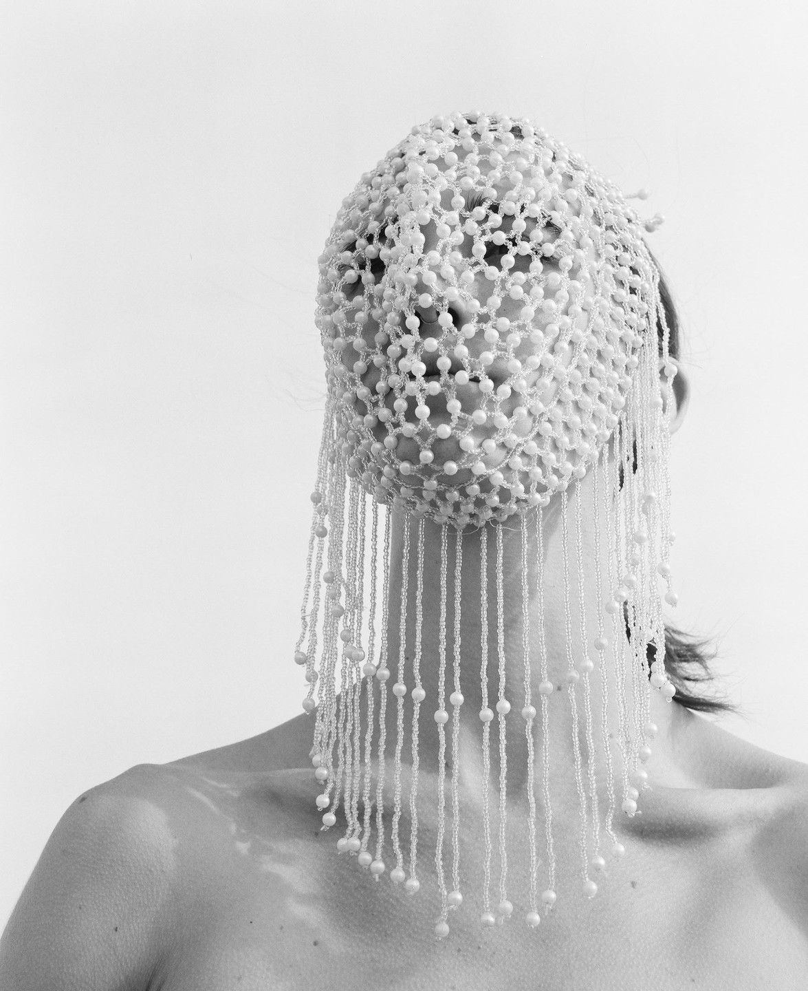 A woman wears a beaded veil that covers her face and extends down to her chest.