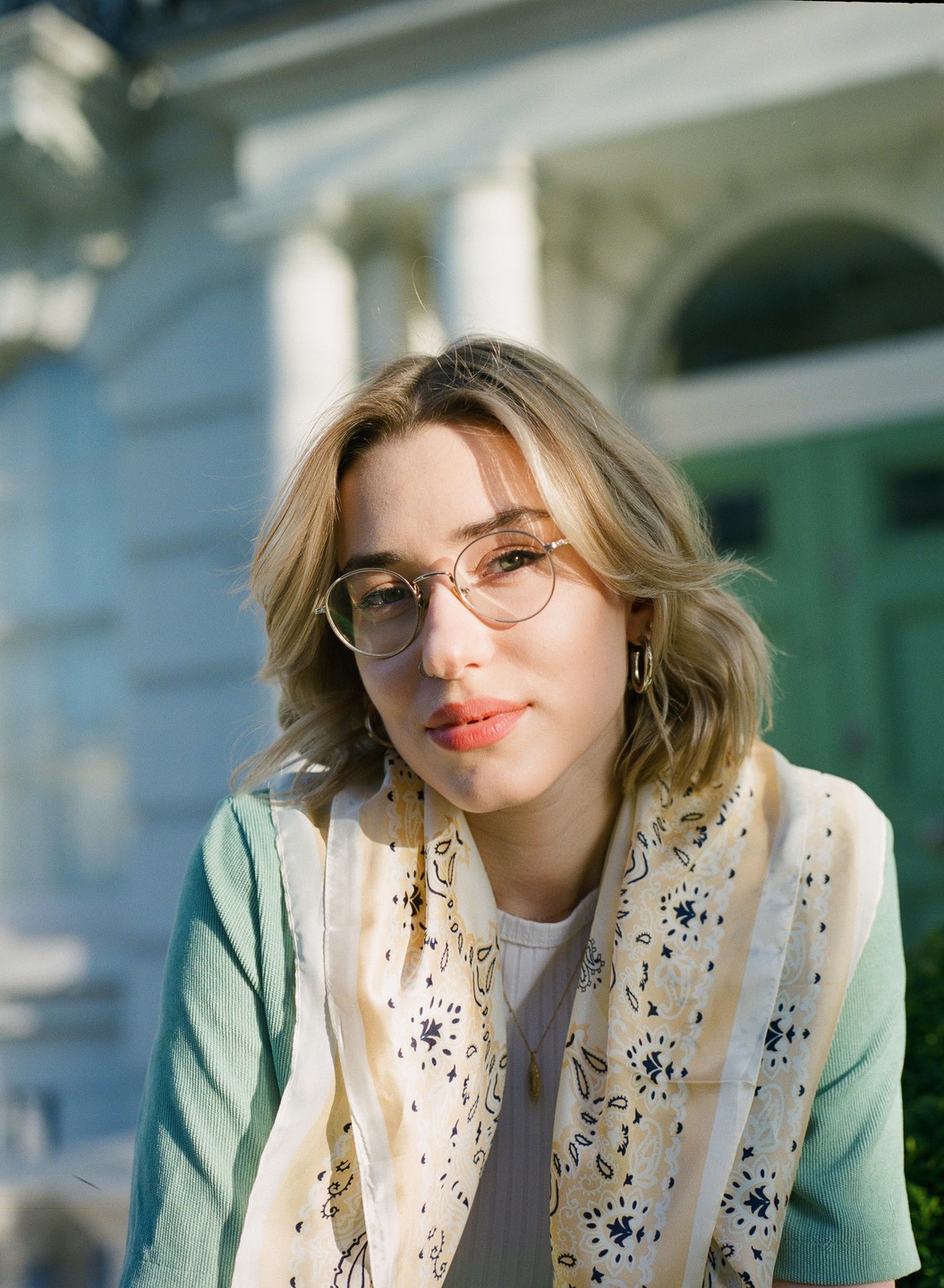 A woman with glasses and a patterned scarf looks at the viewer.