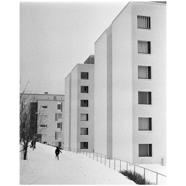 A person walks on a snow-covered path between tall buildings on a winter day.
