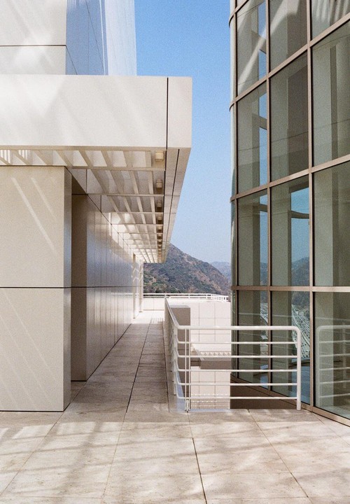 A modern building with a glass facade and a white railing overlooks a mountain.